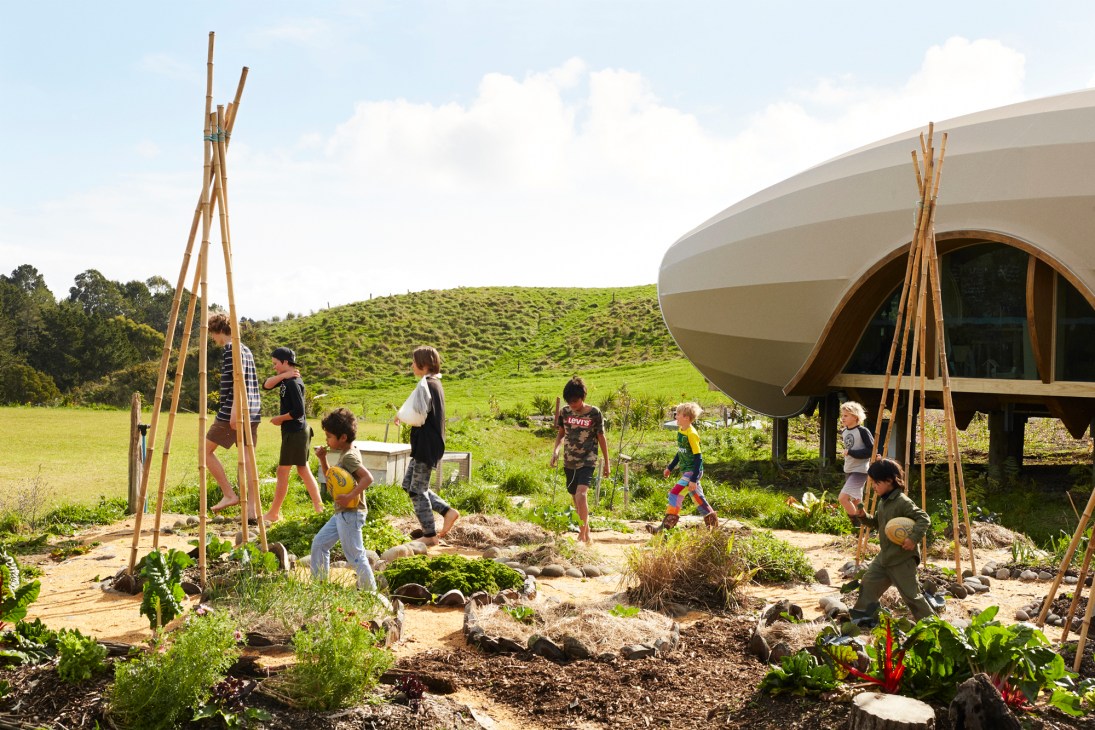Children playing and working in gardens around modern pod-shaped school building at Green School New Zealand