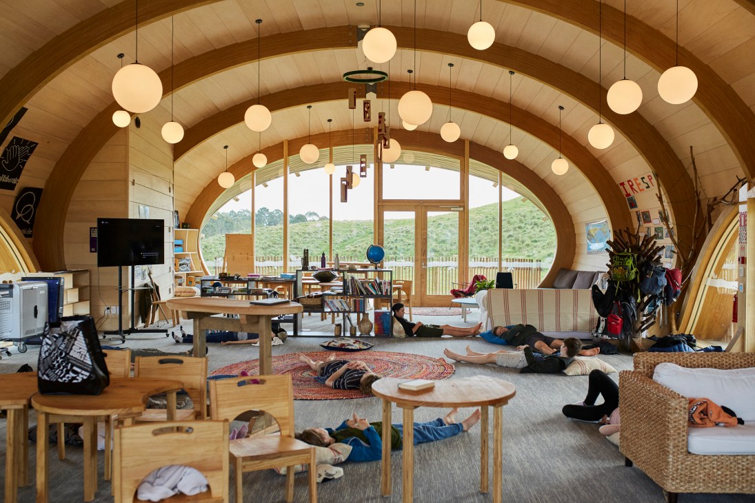 Interior of Green School classroom with curved wooden ceiling, spherical pendant lights, and students relaxing on floor