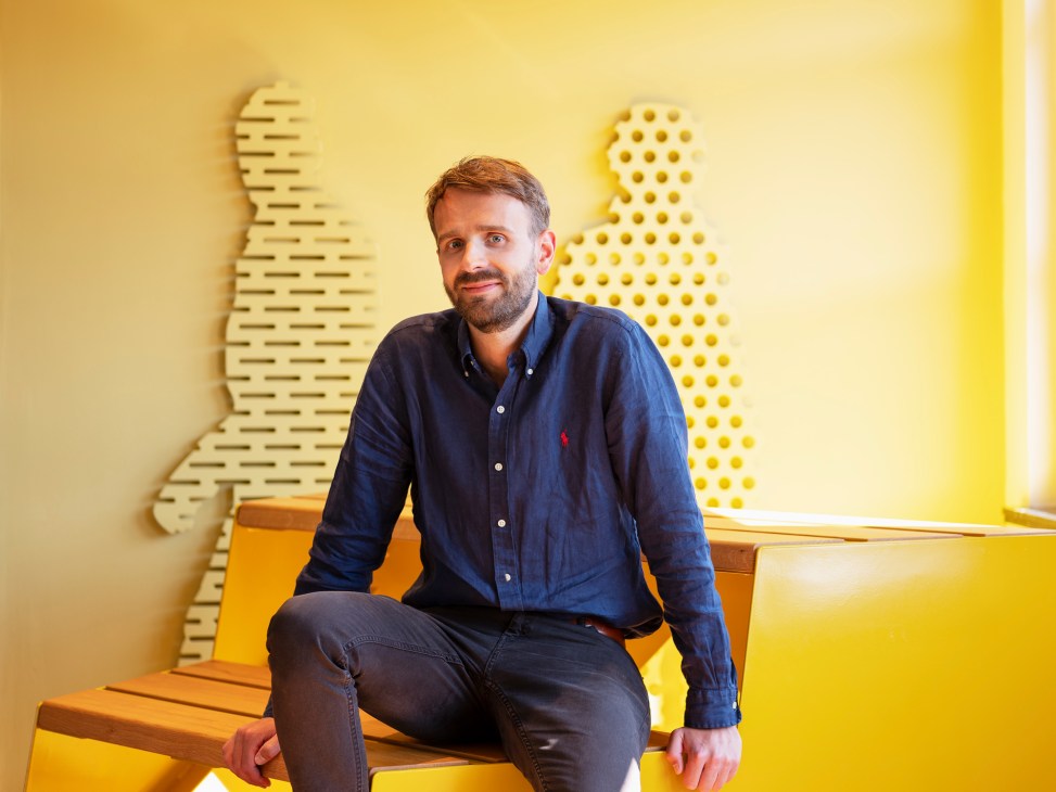 Man in navy shirt sitting on yellow bench against yellow wall with dotted pattern installation.