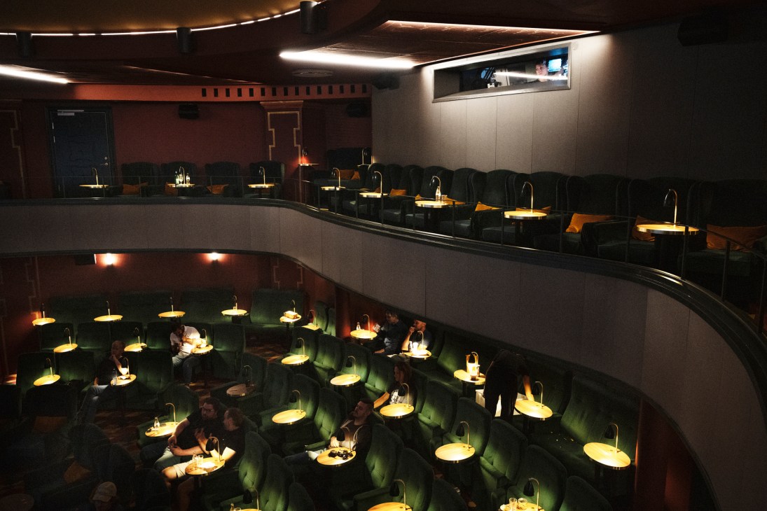 Two-tiered theater at Capitol Bio showing curved rows of dark green velvet seats with individual table lamps