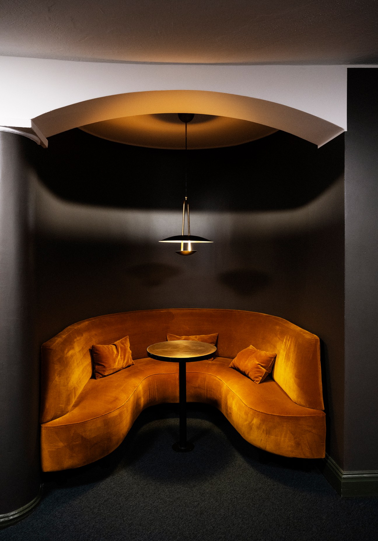 Curved mustard yellow banquette seating in an arched alcove with pendant lighting at Capitol Bio cinema