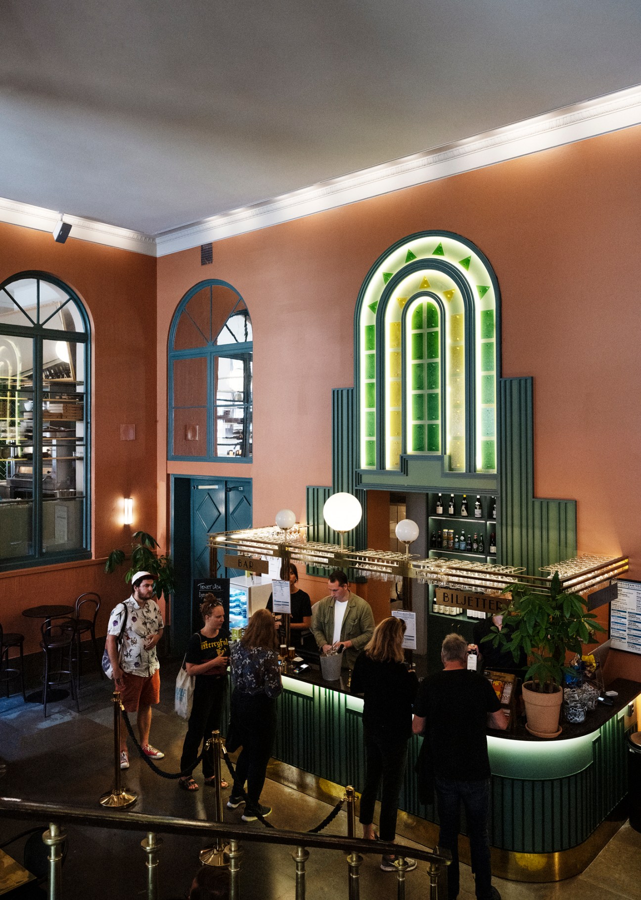 The foyer at Capitol Bio featuring an Art Deco bar area with green lighting, arched windows, and patrons gathered around