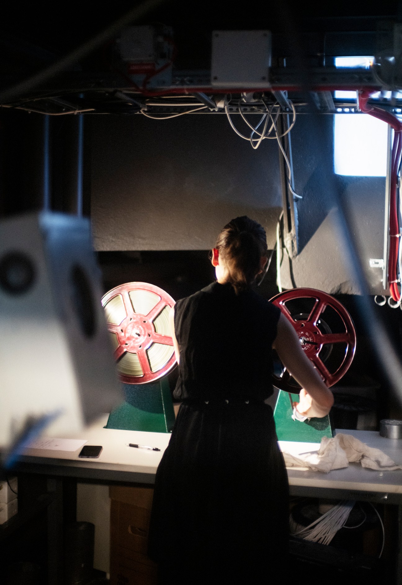 A cinema projectionist operating equipment in the projection booth with film reels visible