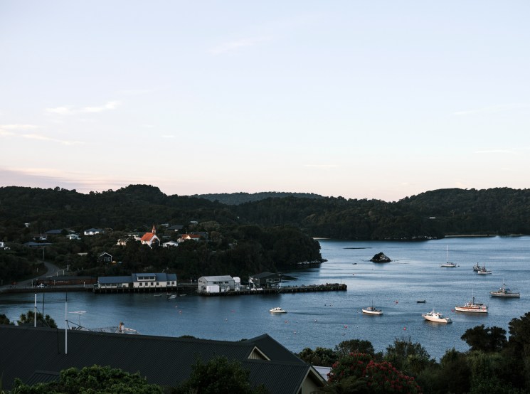 Quiet coastal harbour with boats and a wooded hillside at dusk.