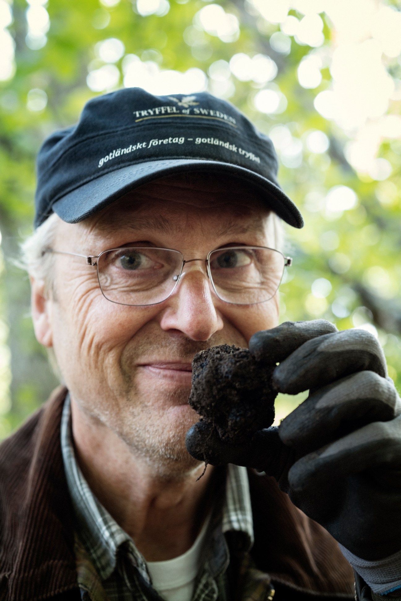 Man wearing glasses and a Tryffel of Sweden cap holds a black truffle in his gloved hand.