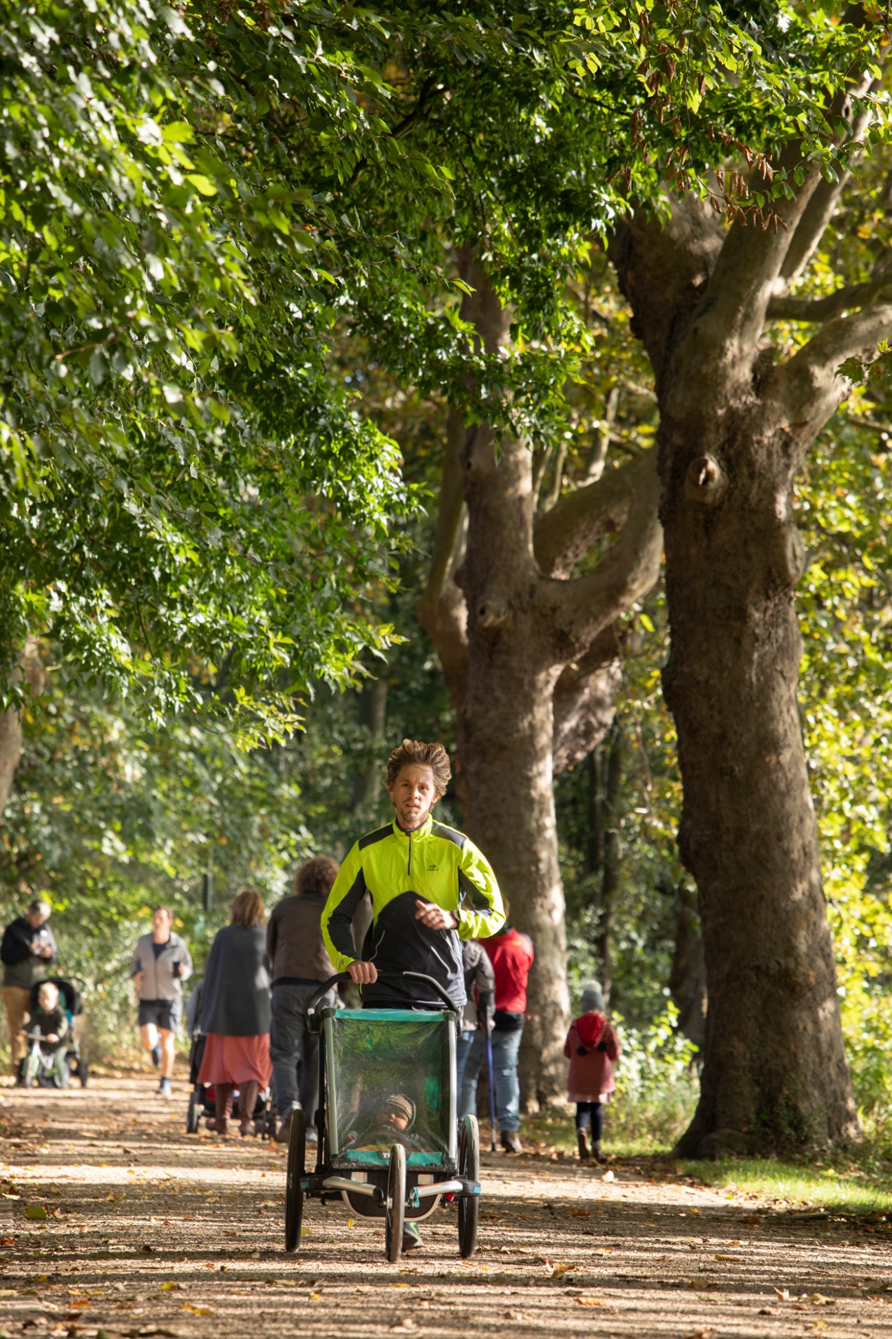 Man jogging in yellow jacket on tree-lined path in Leuven