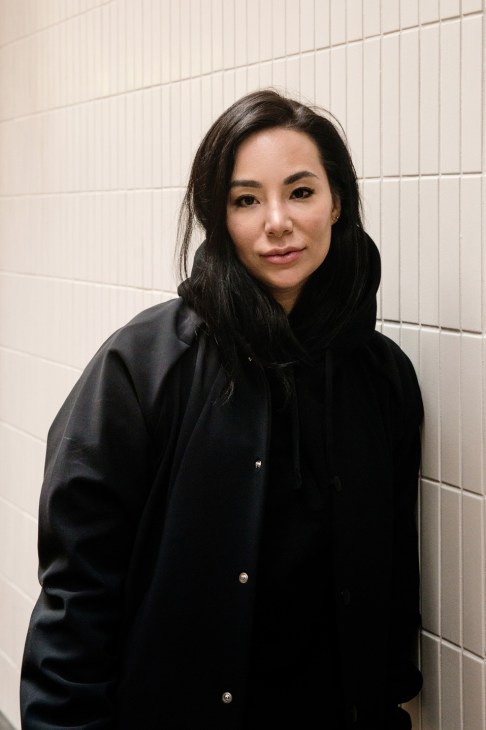 Lindsay Jang, entrepreneur and founder of restaurants and fitness business, poses against a white tiled wall.