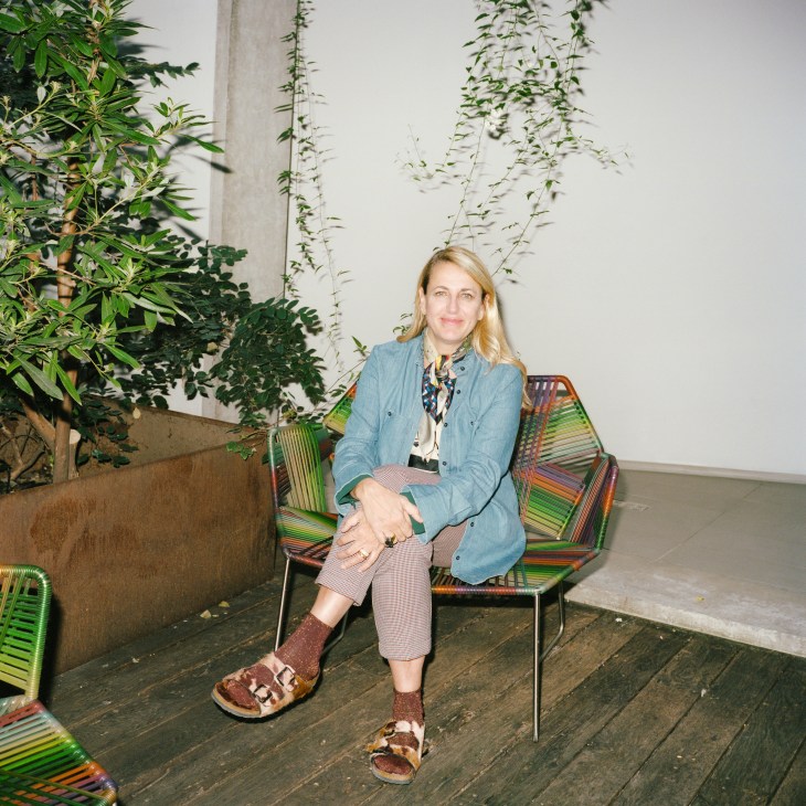 Patricia Urquiola sits on a colorful striped chair in her Milan office, surrounded by hanging plants.