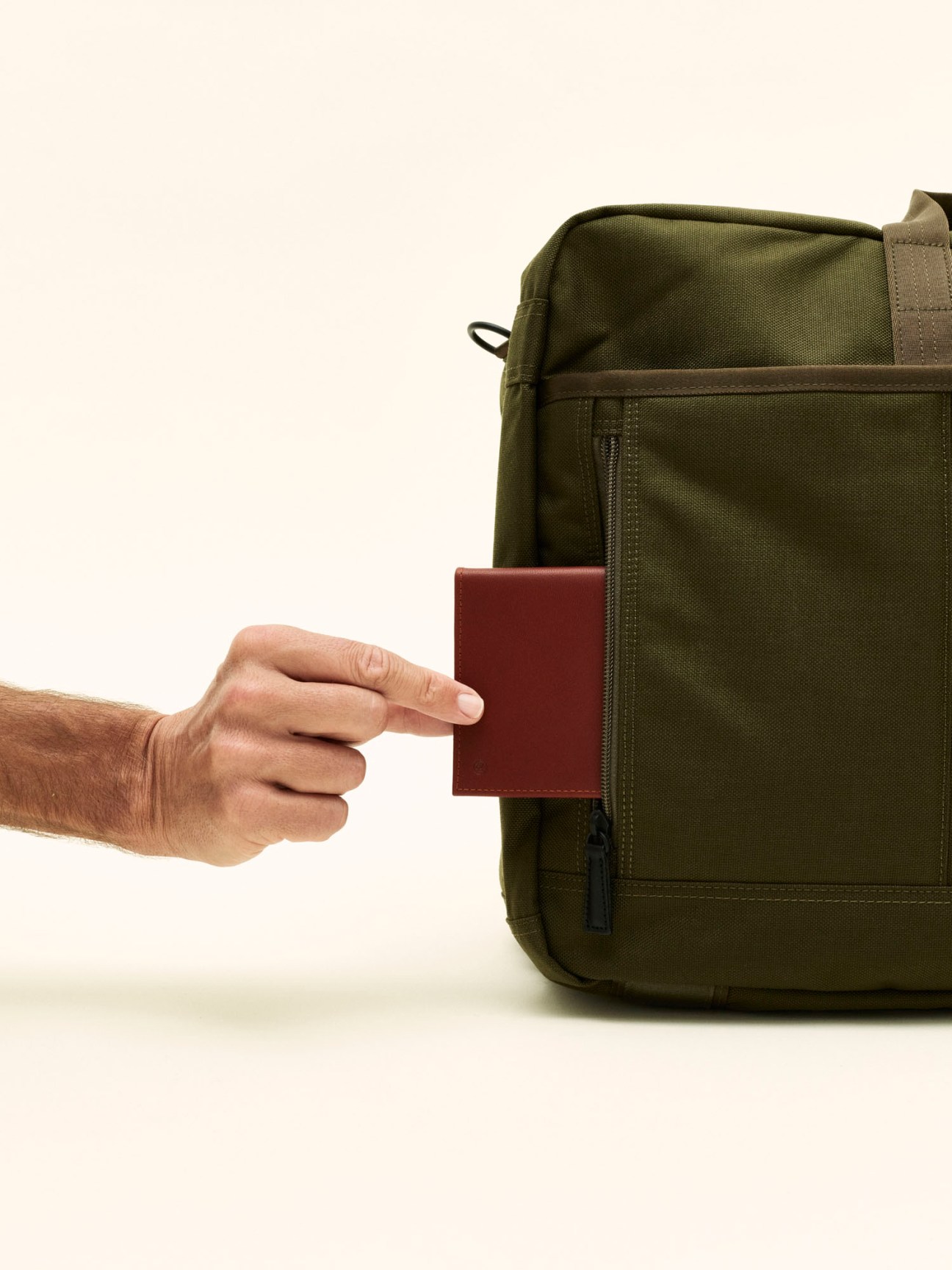 Hand placing red passport into olive green Porter tote bag exterior pocket