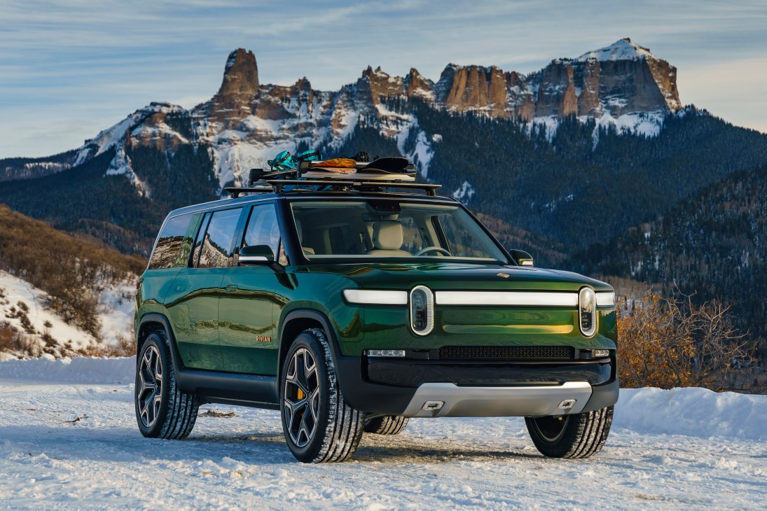 Green SUV with roof cargo parked in snowy landscape with snow-covered mountains in background