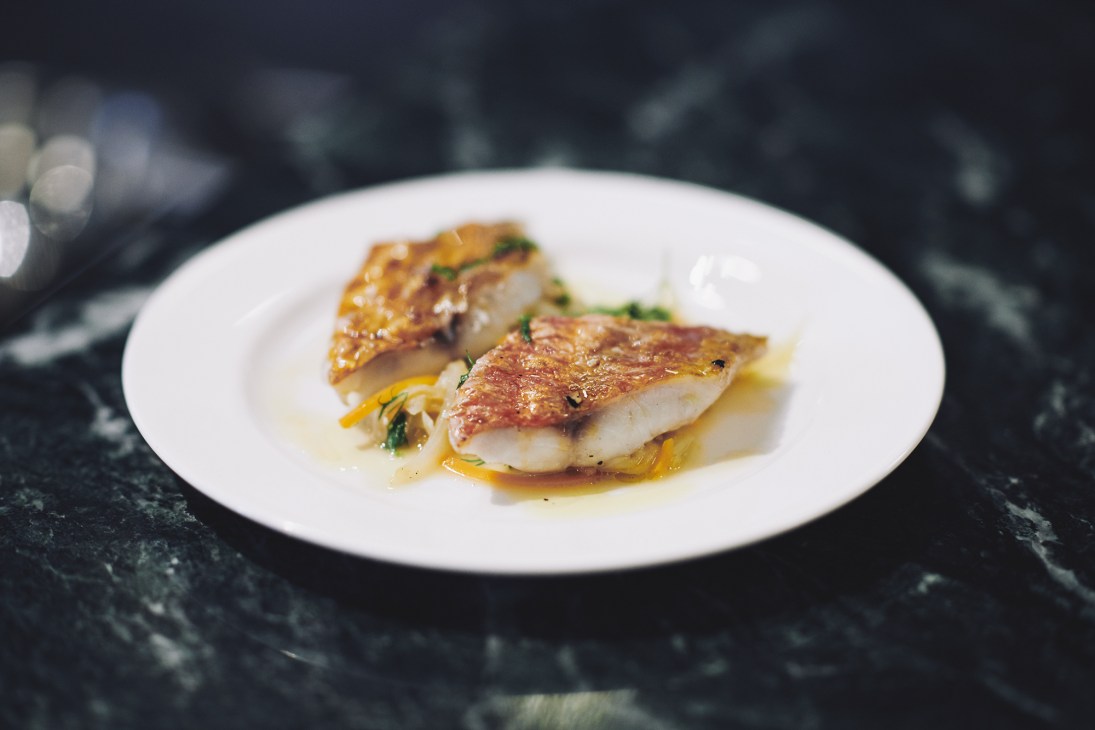 Two seared fish fillets with golden-brown skin on a white plate at Brat restaurant