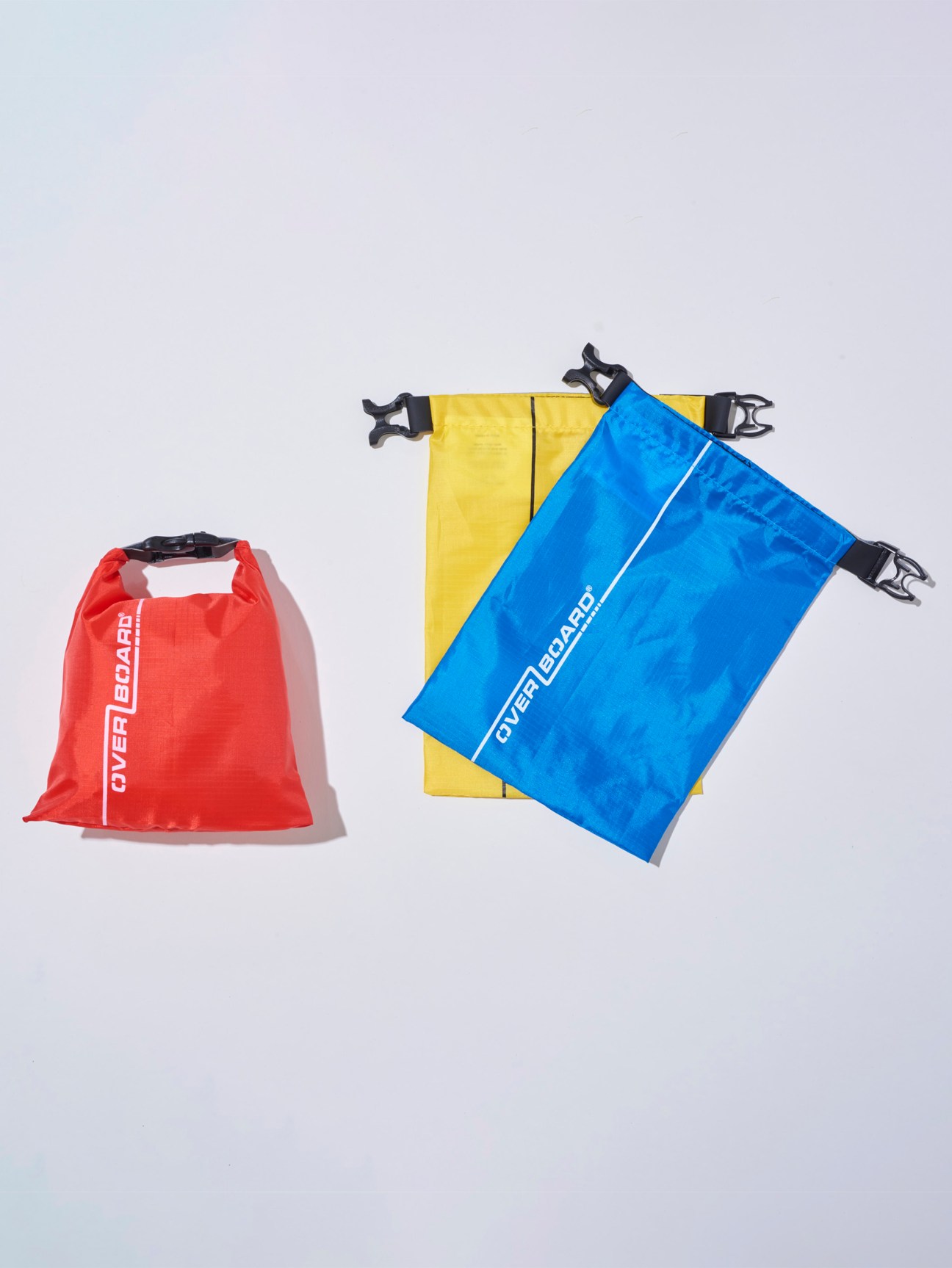 Red and blue waterproof dry bags by Overboard with black buckle closures displayed against a light background.