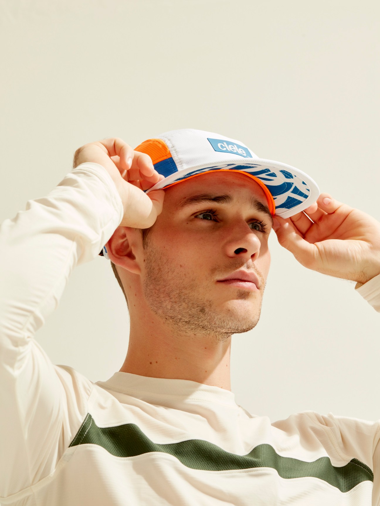 Male model adjusting a Ciele Athletics GoCap in orange and white with blue logo details.