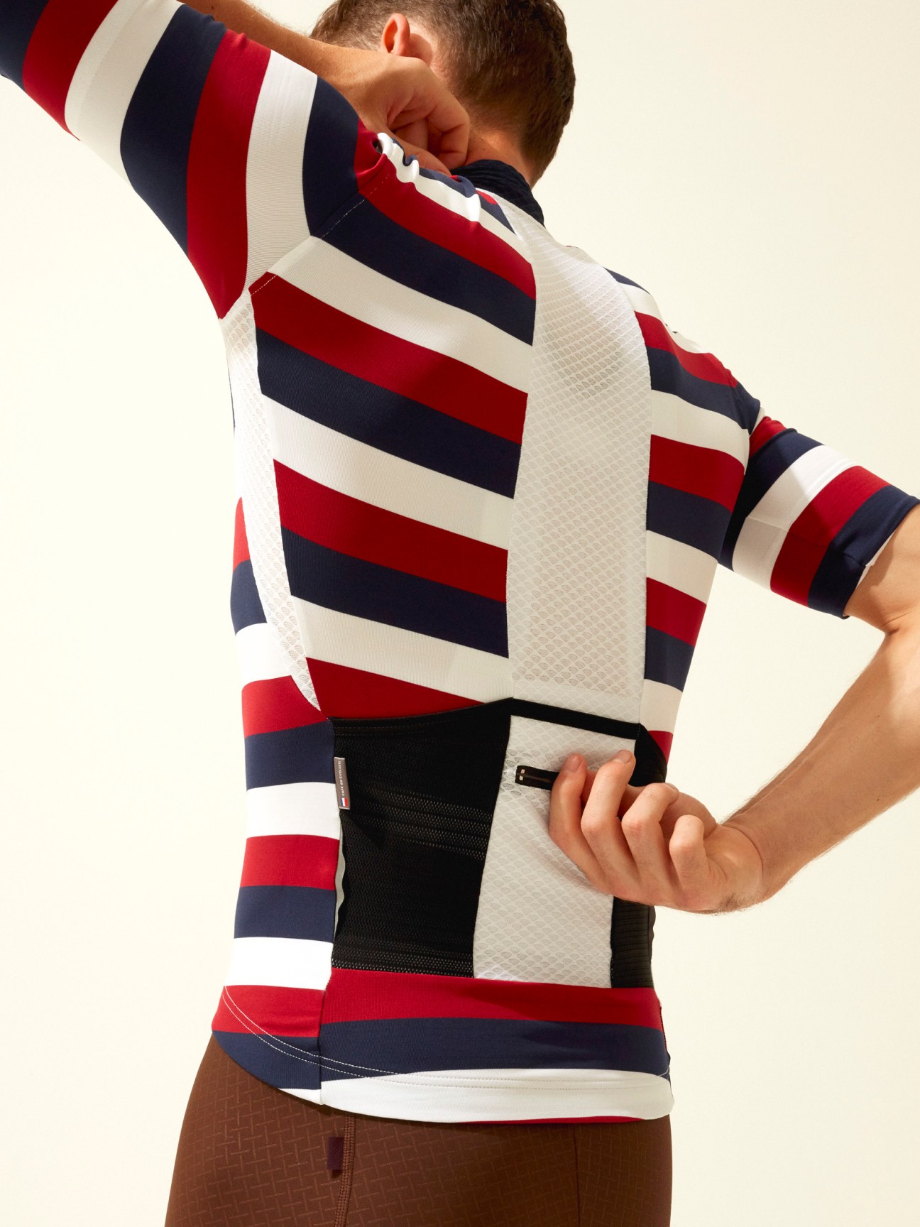 Male cyclist wearing a red, navy and white striped cycling jersey with mesh panels.