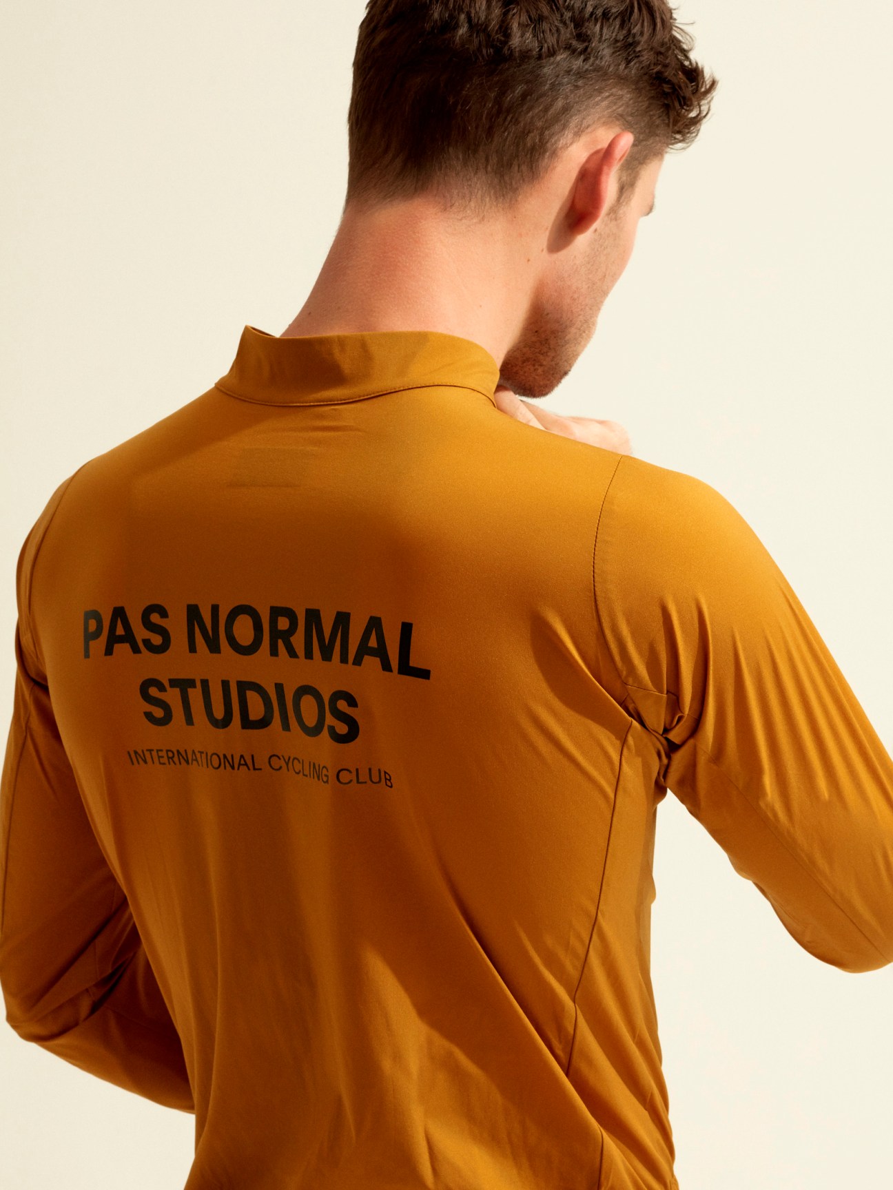 Man wearing mustard-yellow Pas Normal Studios cycling jacket with International Cycling Club text on back.
