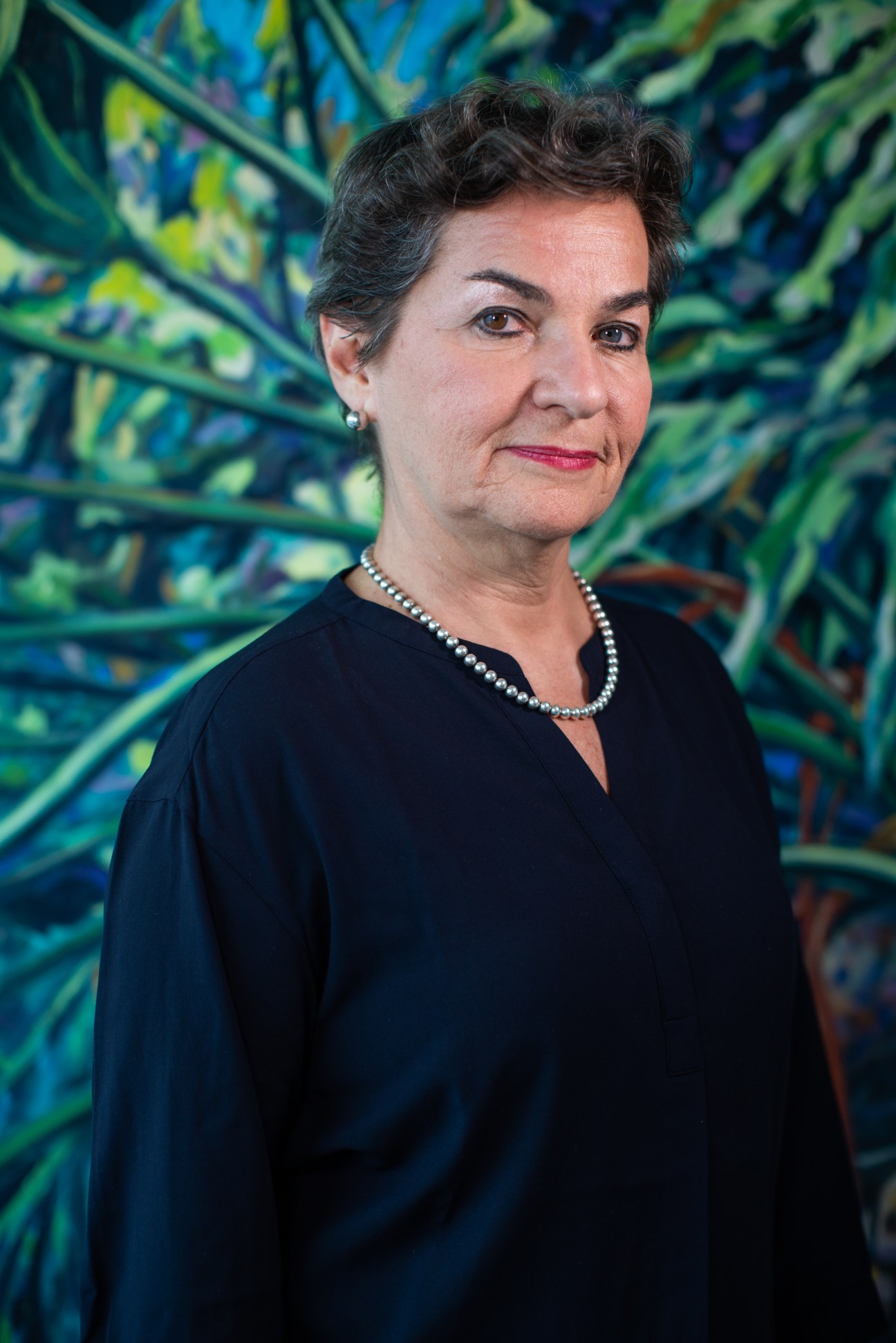 Christiana Figueres wearing a dark outfit with pearl necklace against colorful background