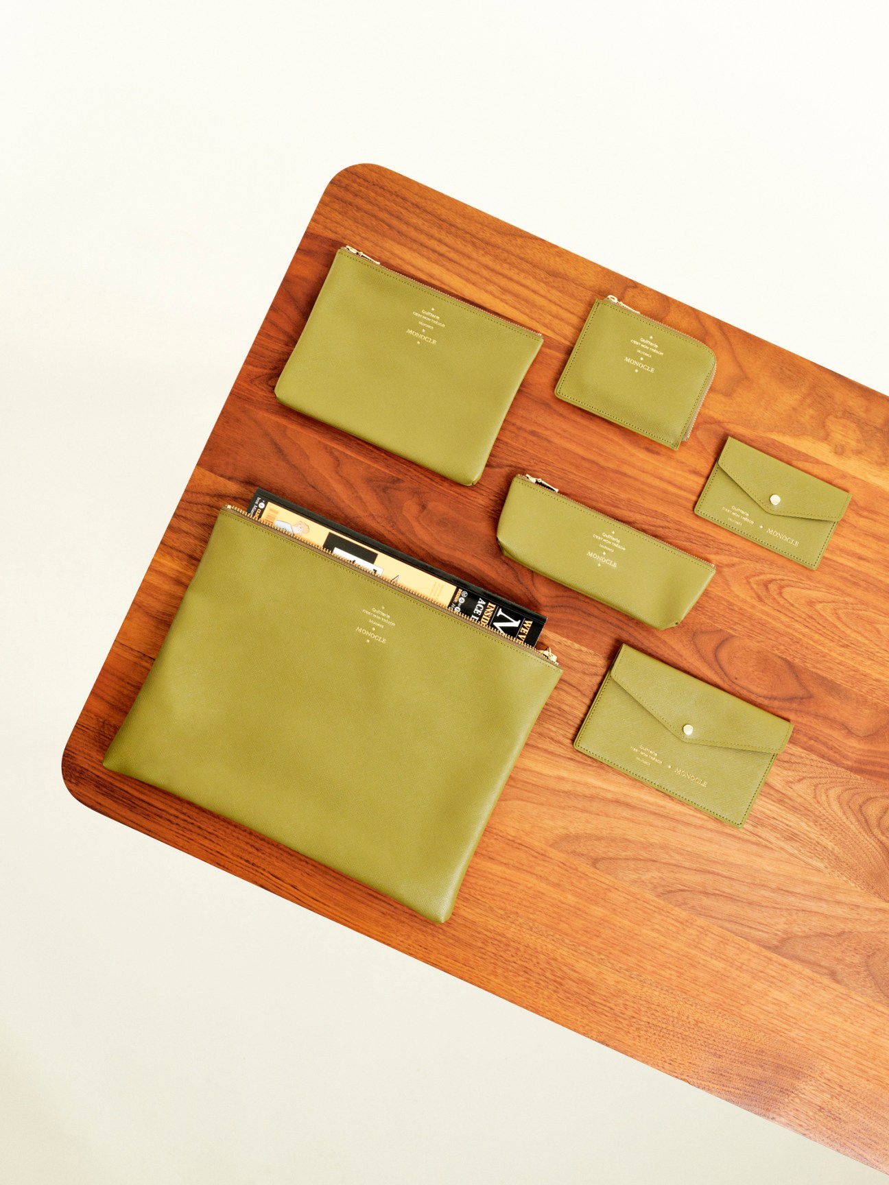 Collection of lime-green leather pouches by Delfonics x Monocle arranged on wooden surface.