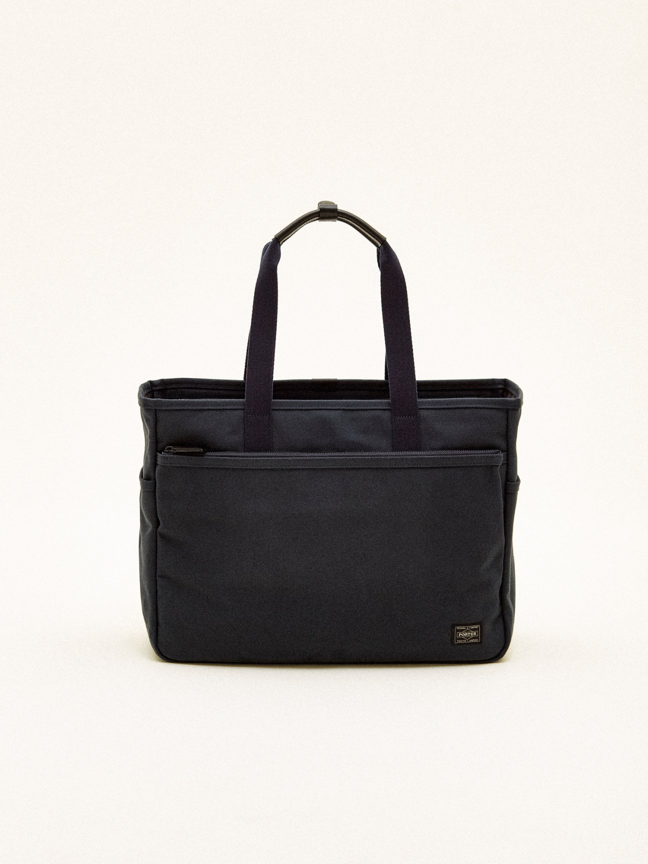 Black Porter x Monocle zip tote bag with front zipper pocket and handles against white background