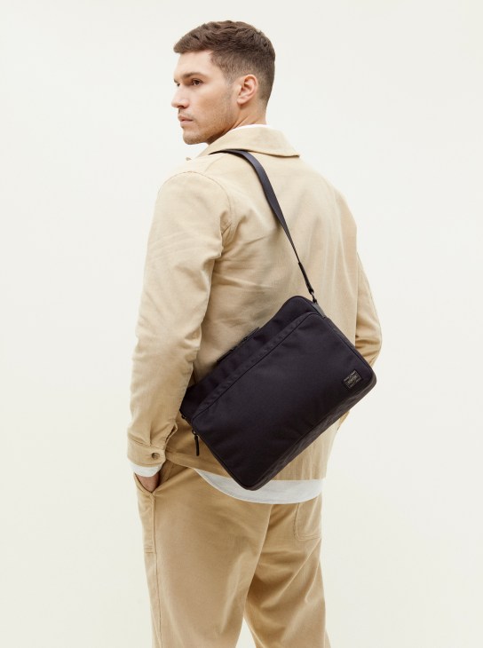 Man wearing beige jacket carrying black Porter x Monocle shoulder bag.