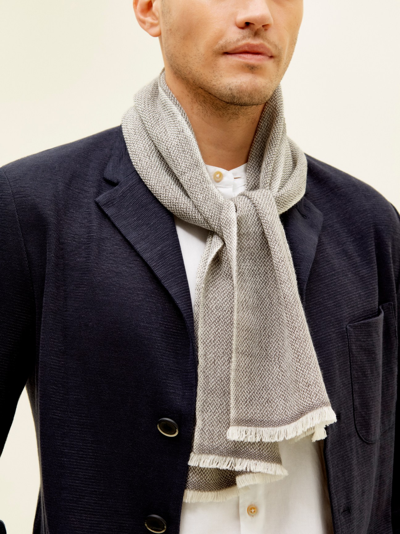 Man wearing navy blazer with narrow merino wool scarf by Monocle in beige.