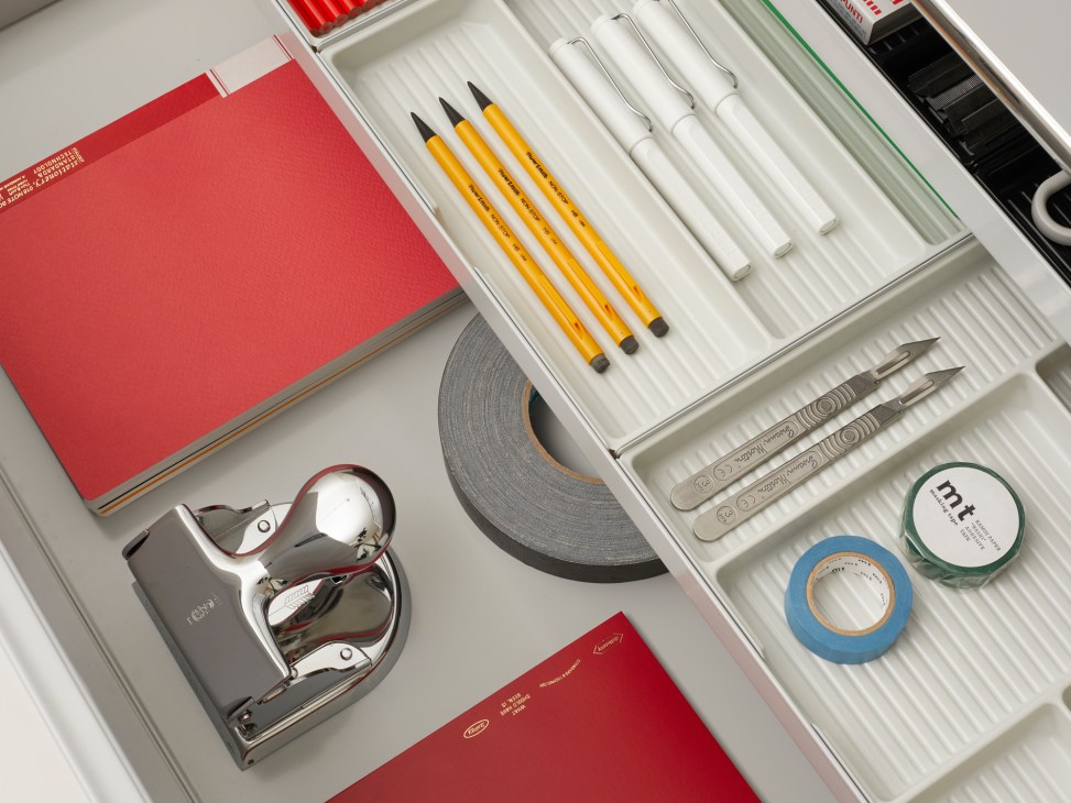 Overhead view of stationery items in white organizer tray including El Casco hole punch, pencils, tape, and scissors.