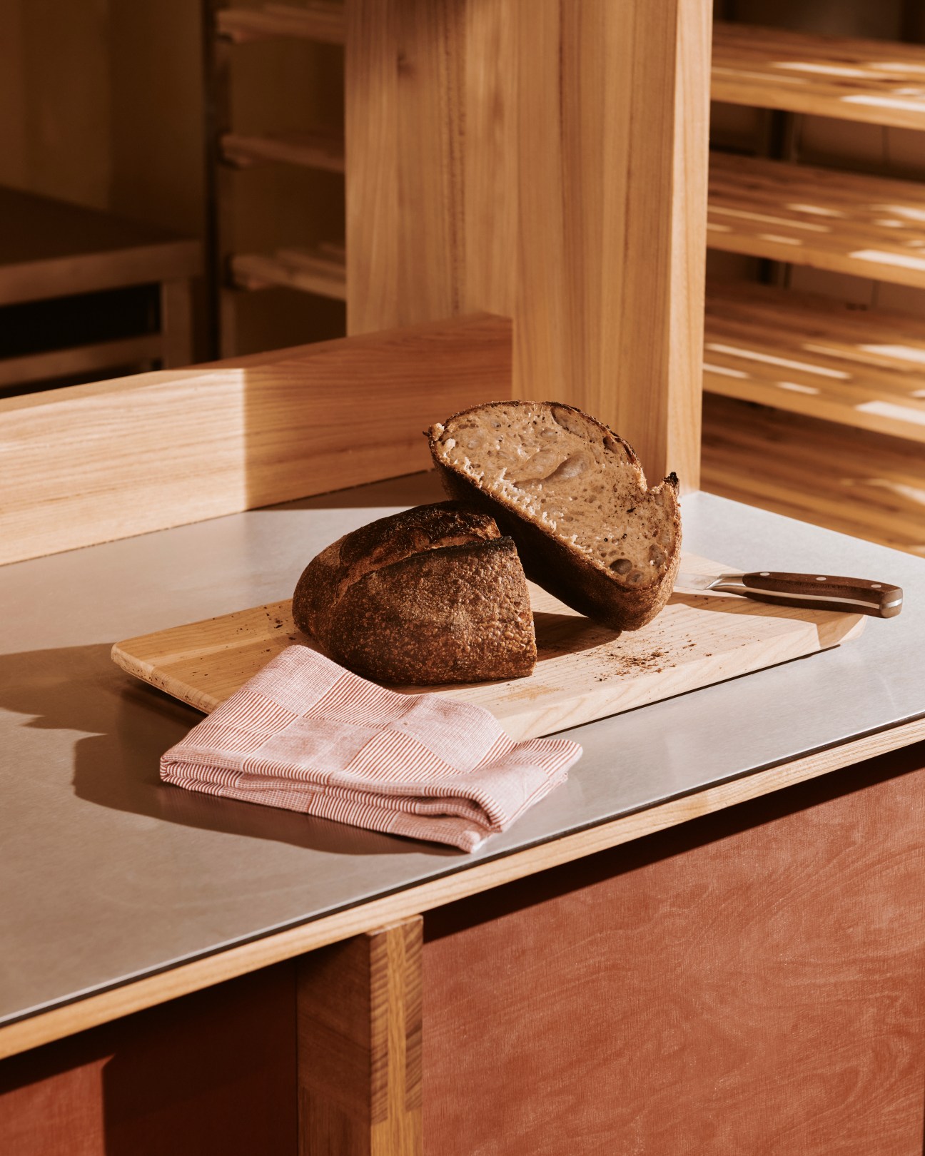 Dark sourdough bread loaf cut in half on wooden cutting board with striped kitchen towel
