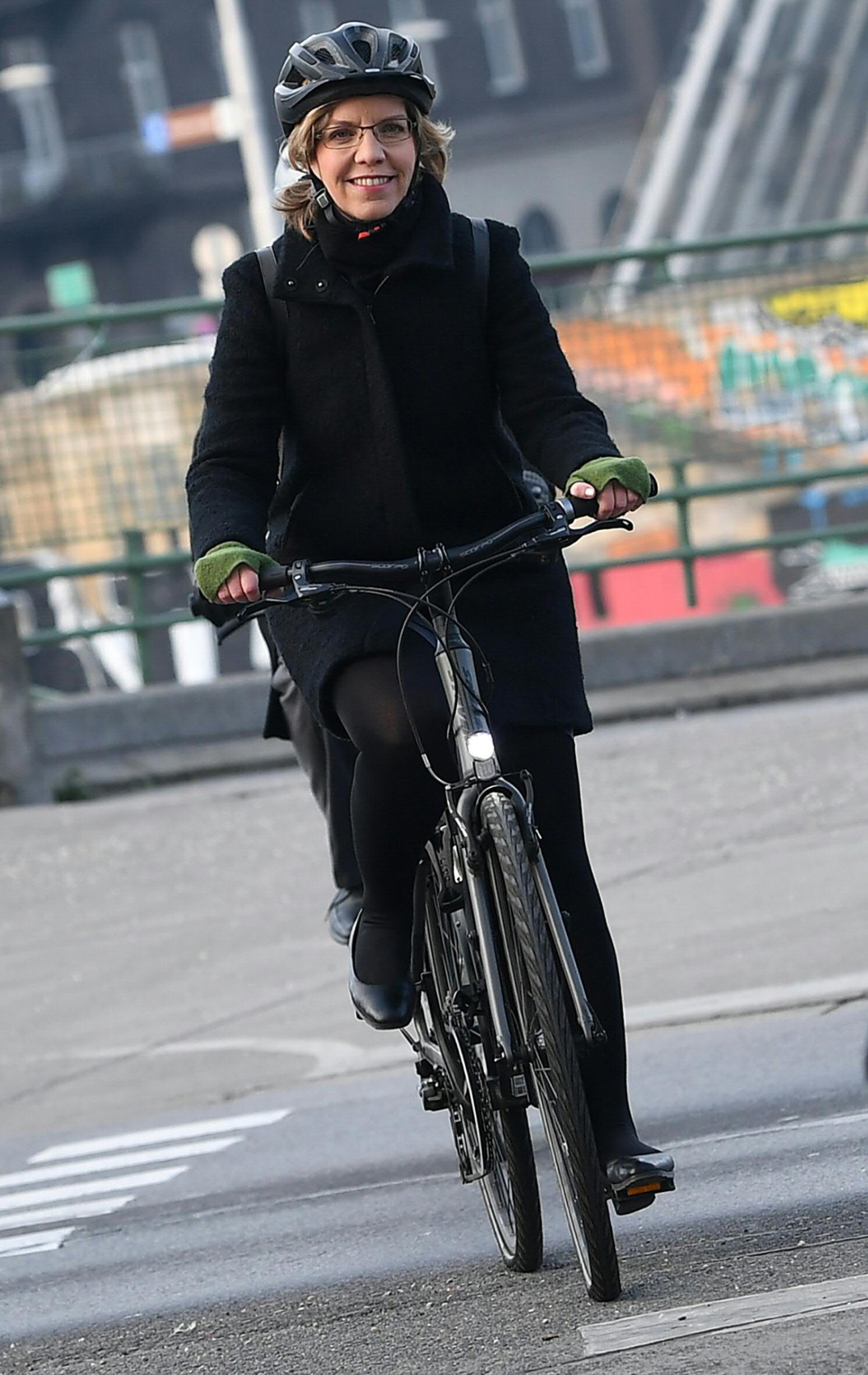 Leonore Gewessler riding a bicycle while wearing a helmet and dark coat on a city street