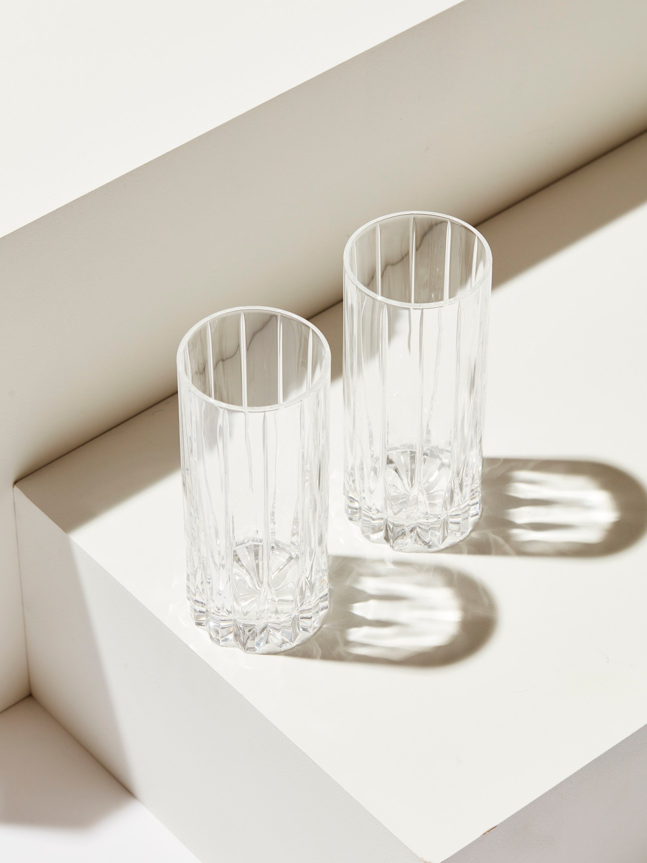 Two clear crystal glasses with vertical ridged pattern and decorative cut base sitting on white surface