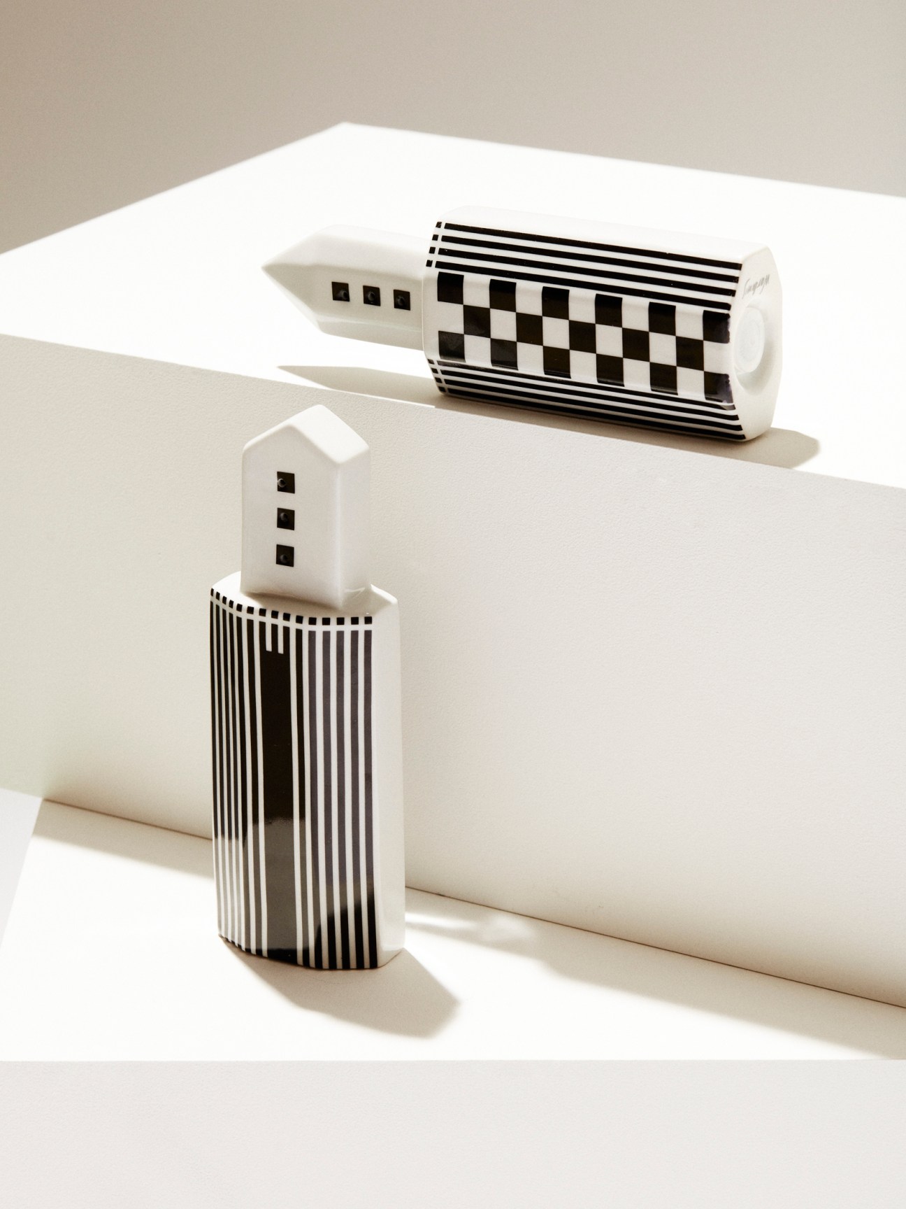 Two white ceramic salt and pepper shakers with black geometric patterns including stripes and checkerboard designs