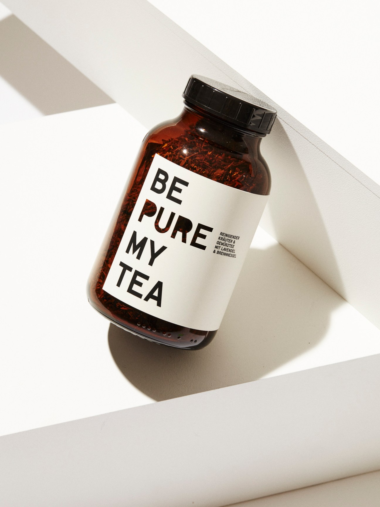 Brown glass jar with black lid labeled BE PURE MY TEA containing loose tea leaves