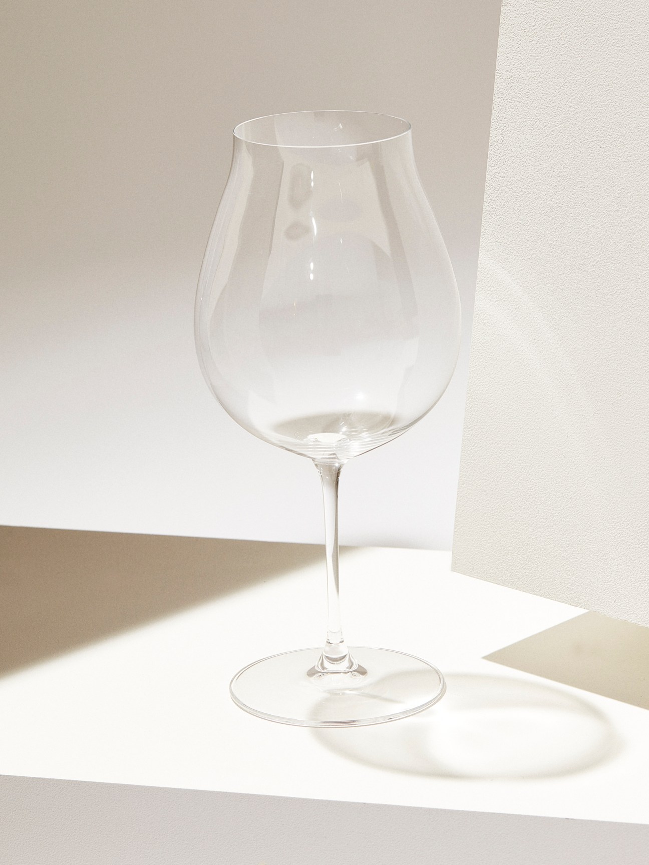 Clear glass wine glass with bulbous bowl and long stem against neutral background