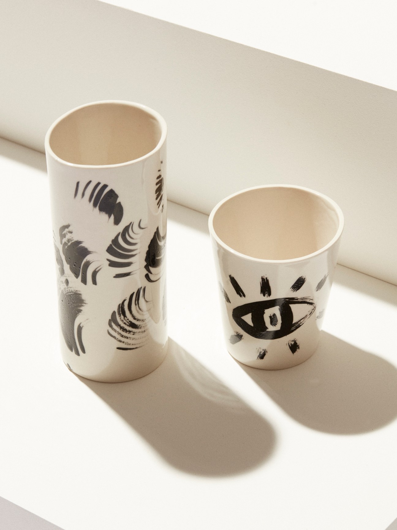 Ceramic vase and cup with black brushstroke designs by Andrea Kollar on white surface