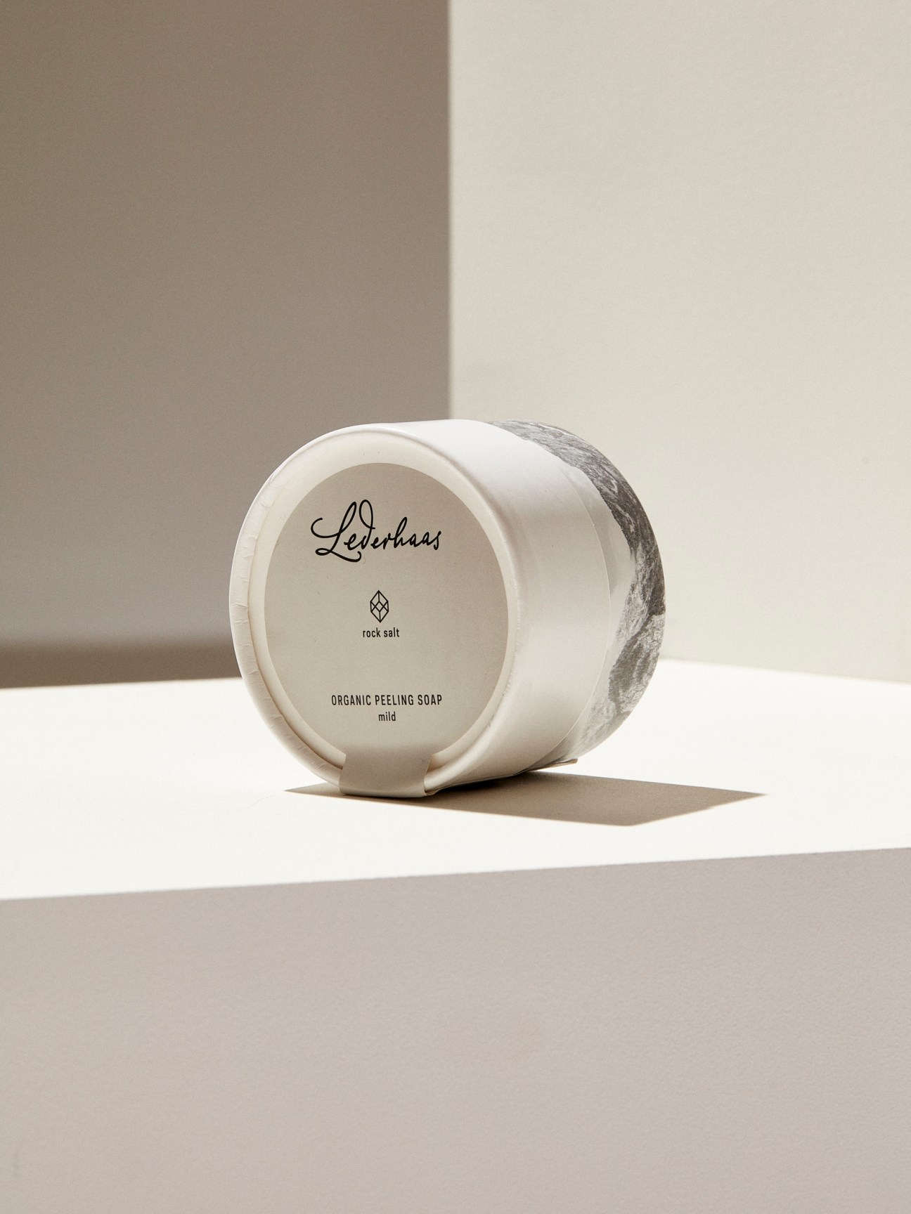 White cylindrical container of Lederhaas organic peeling soap with rock salt on neutral background