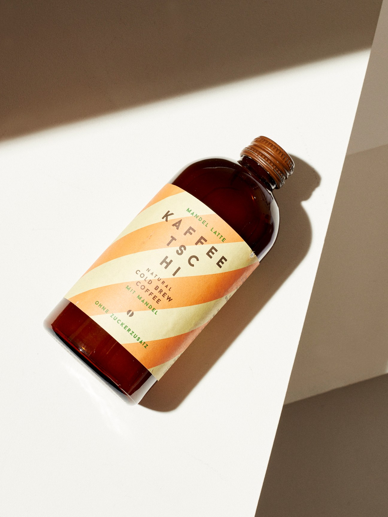 Amber glass bottle of Kaffeetschi cold-brew coffee with colorful striped label on white surface