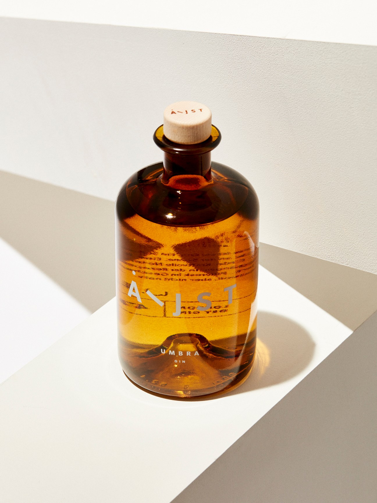 Amber glass bottle of Aeijst gin with cork stopper on white surface