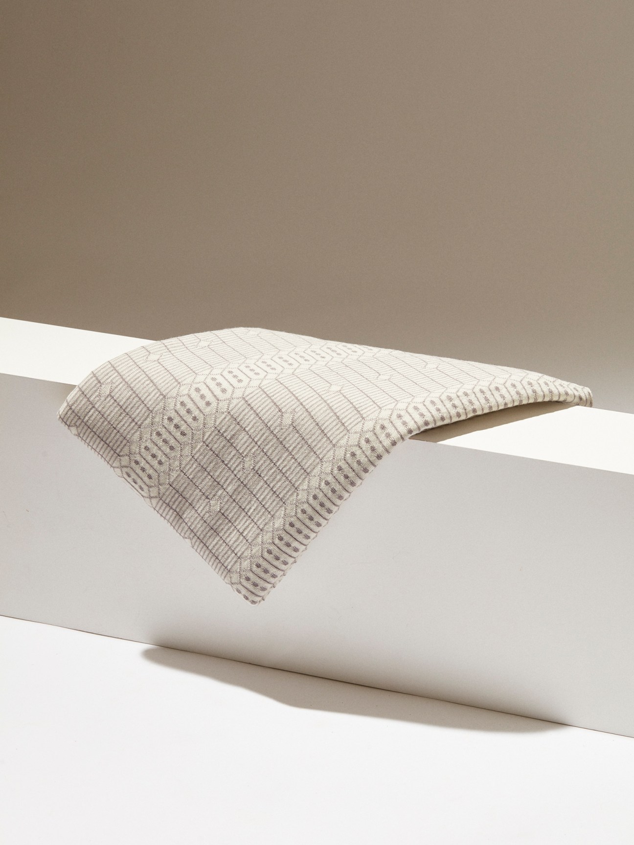 Beige textured blanket with geometric pattern draped over white cylindrical surfaces