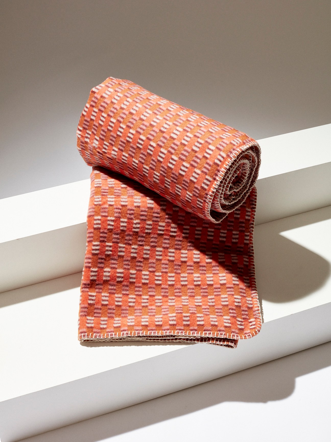 Orange and burgundy patterned woven blanket with geometric design partially unrolled on white surface