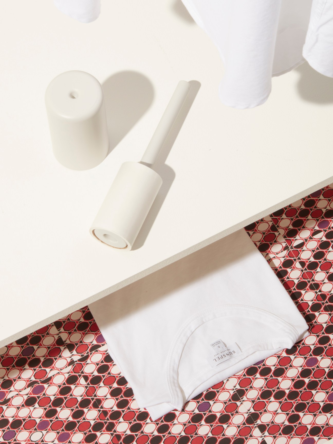 White lint roller and folded scented drawer liner on white shelf above red geometric patterned surface