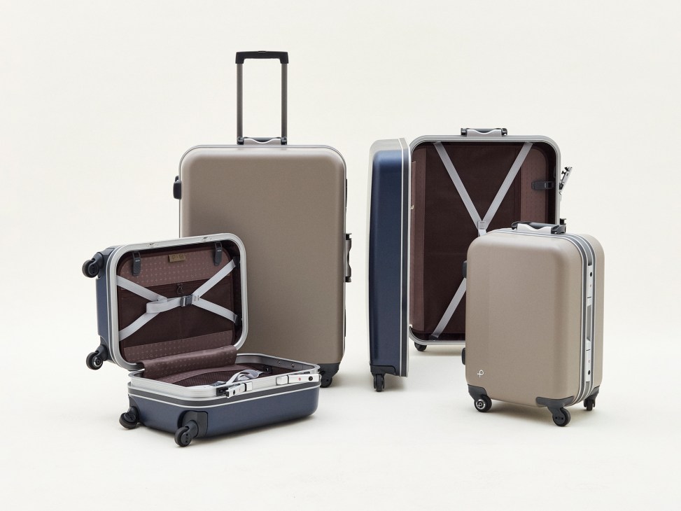 Proteca x Monocle Equinox Light U suitcases in beige and navy with open carry-on showing interior packing straps and luggage belt.