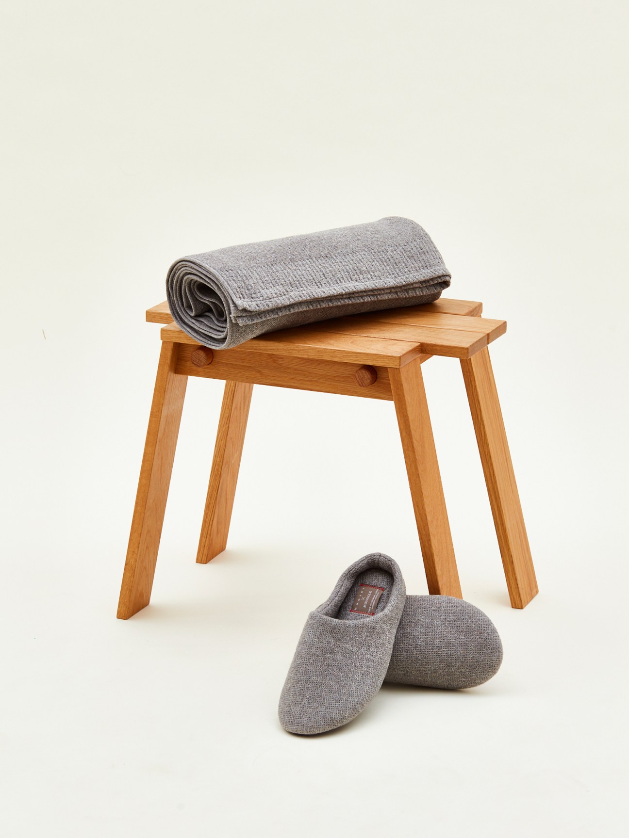 Grey cotton towel rolled on wooden stool with matching grey slippers below