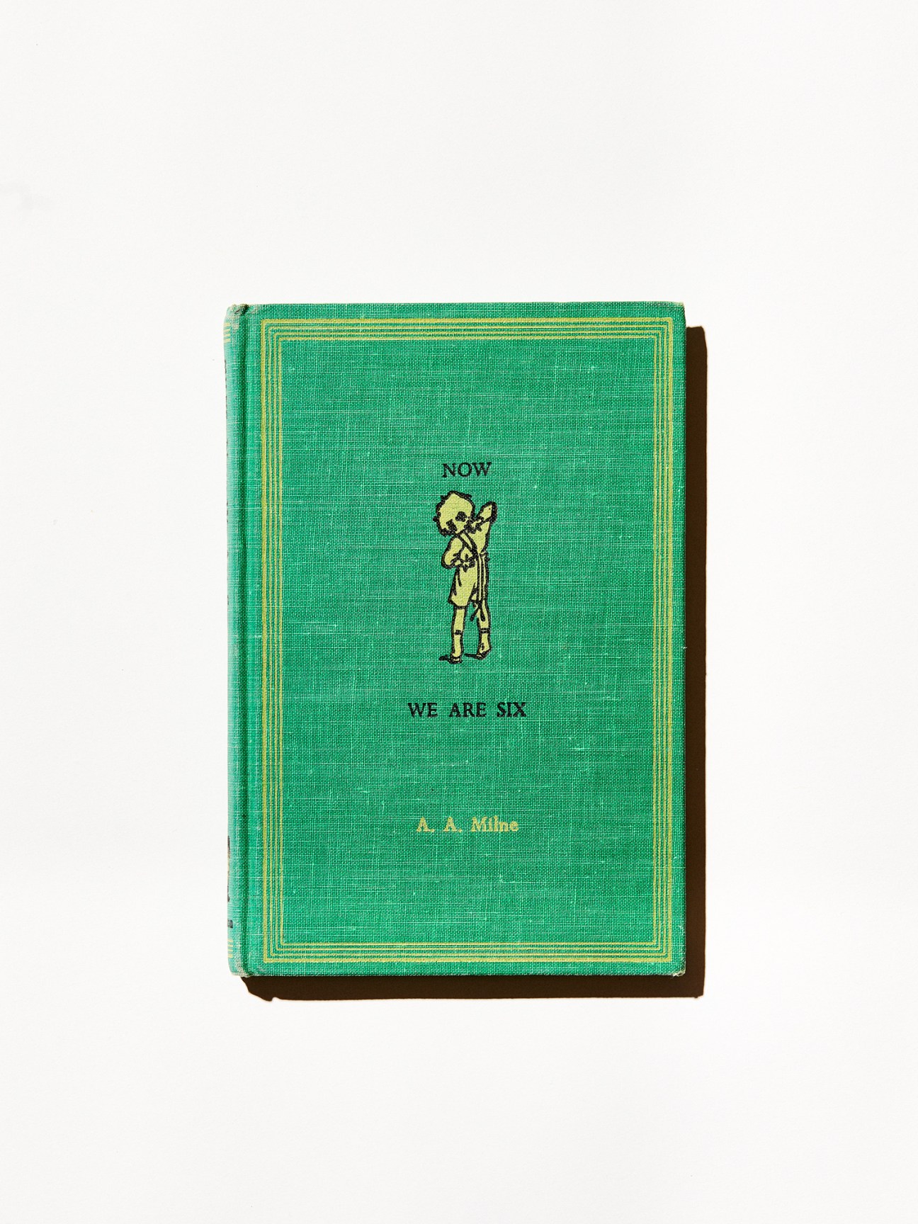 Green cloth-bound book cover showing Now We Are Six by A.A. Milne with Christopher Robin illustration