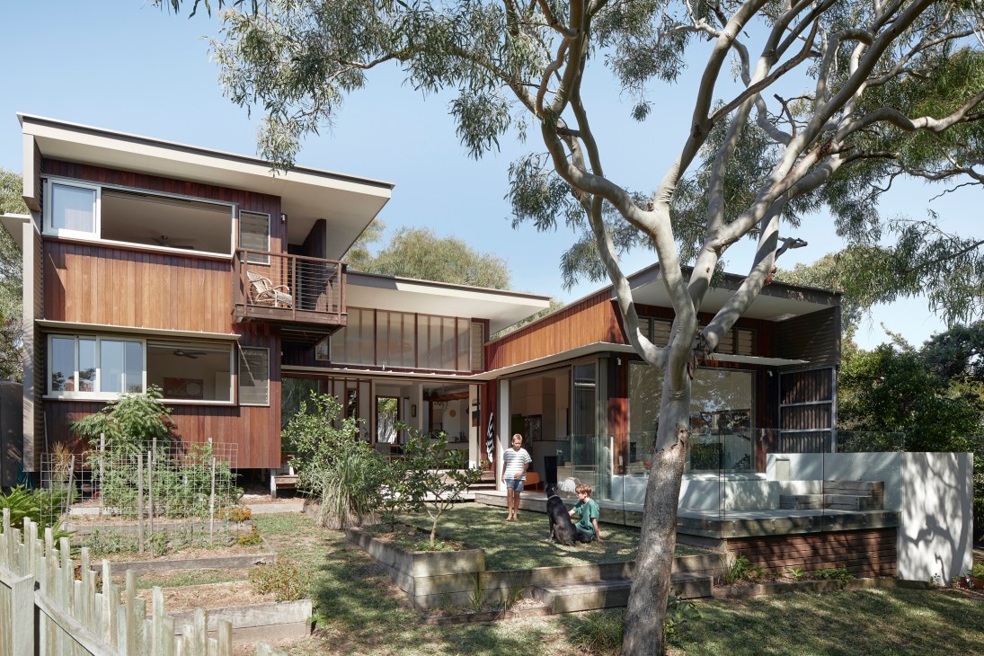 Modern two-story house with timber cladding, large windows, and outdoor deck surrounded by eucalyptus trees