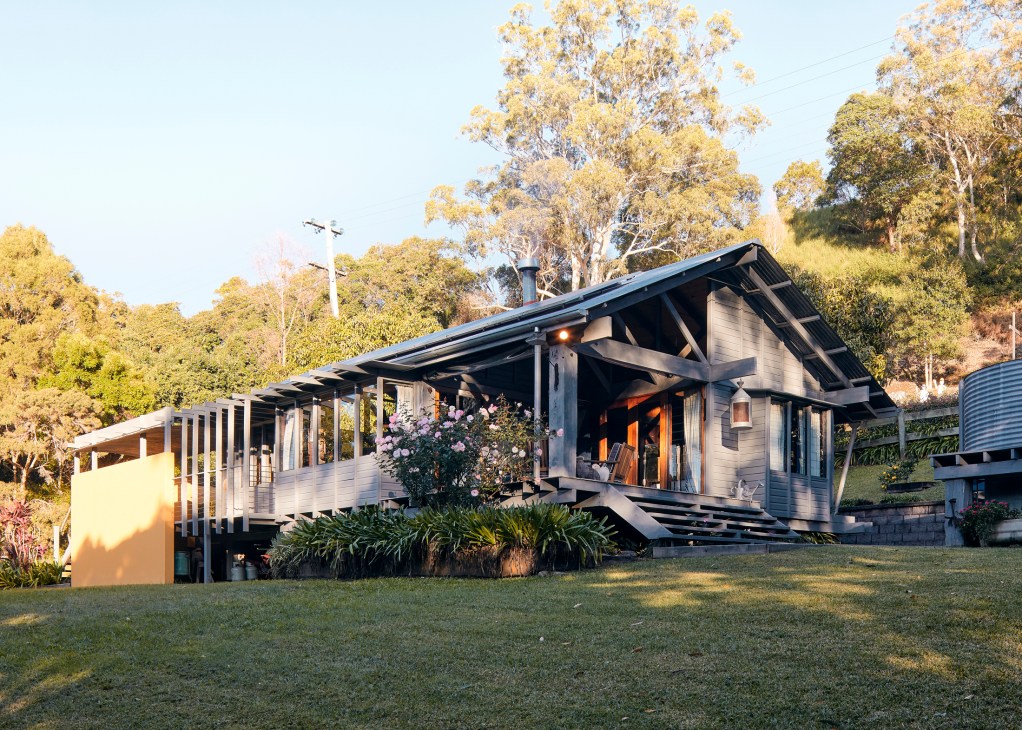 Modern timber house with covered deck and large windows surrounded by trees and lawn at golden hour