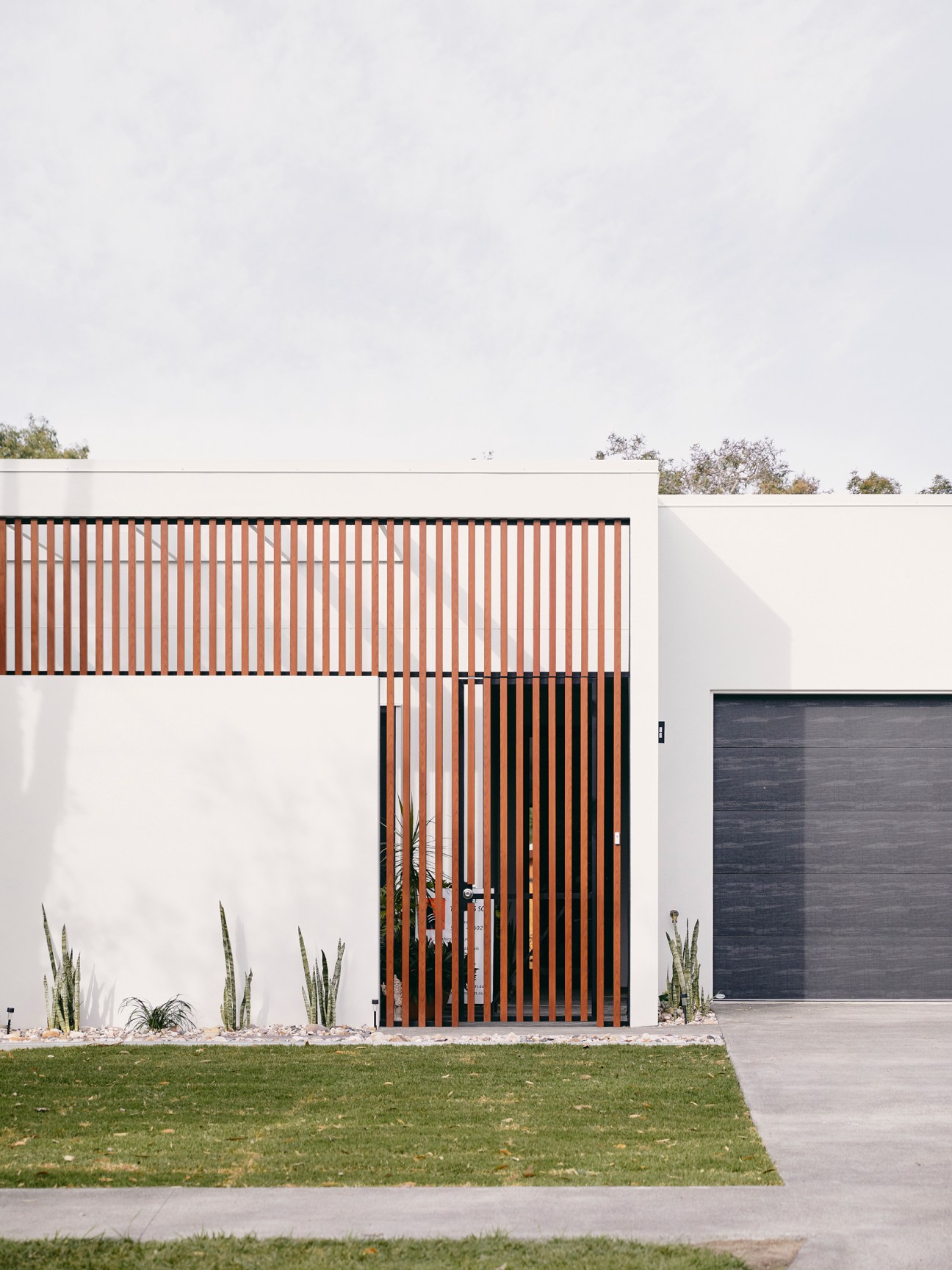 Modern white house with vertical timber slat screening and dark garage door