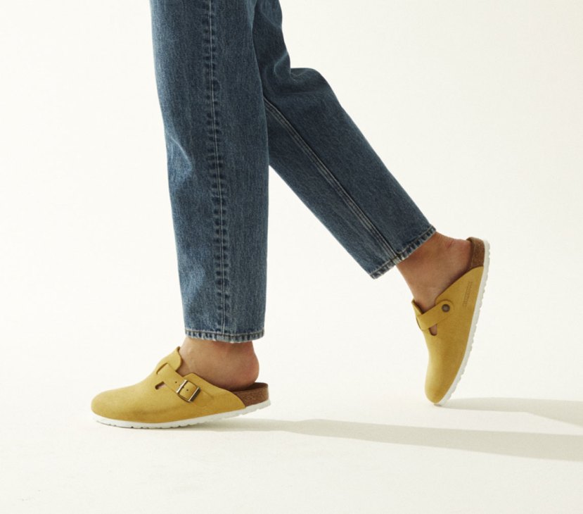 Person wearing blue jeans and yellow Birkenstock sandals with buckle strap.