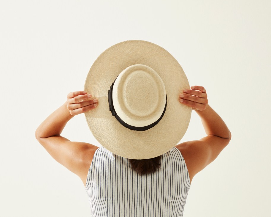 Person wearing a striped ribbed tank top and straw hat with black band by Celine.