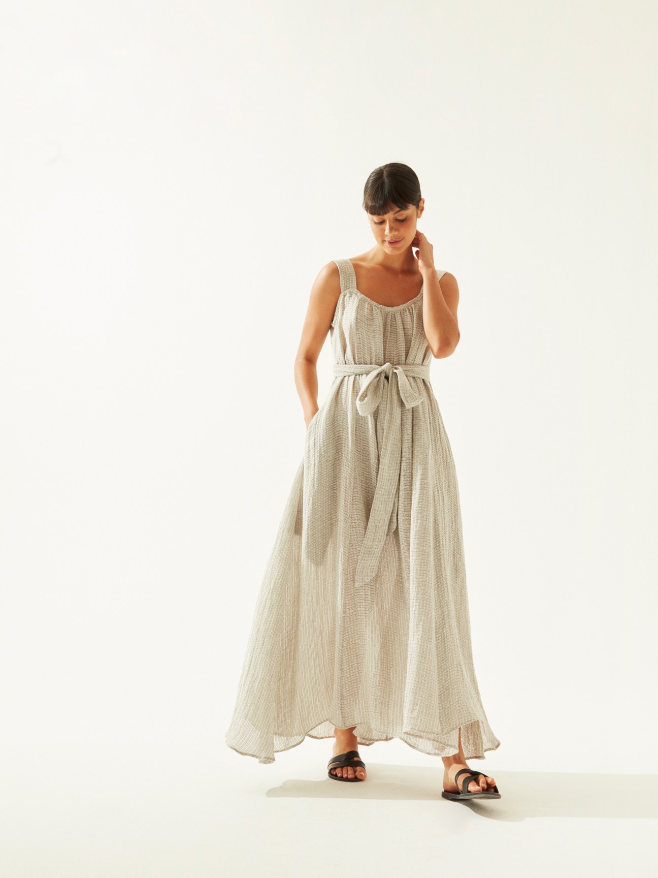 Woman wearing a light beige linen dress by Le Kasha with black sandals by Ancient Greek Sandals.