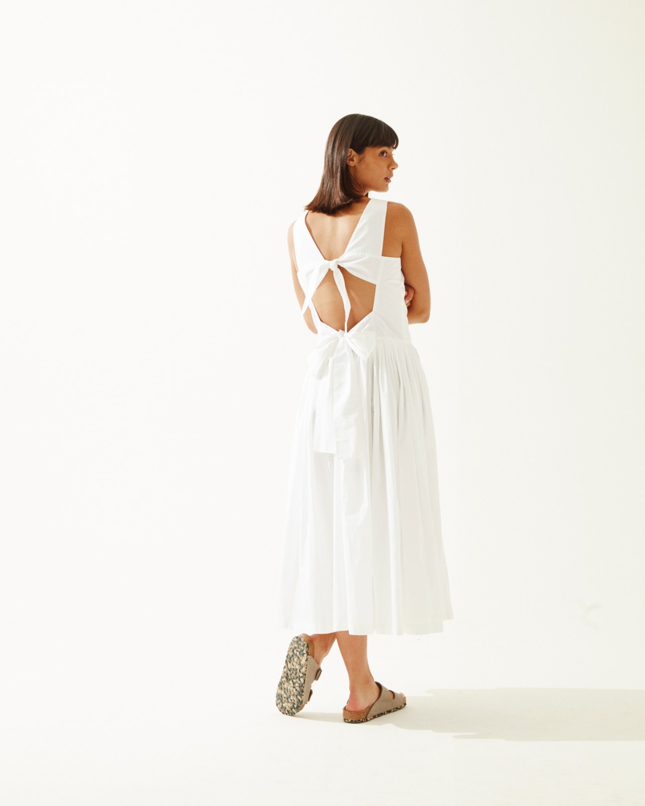 Woman wearing a white sleeveless dress by Sara Lanzi with back cutout and Birkenstock sandals.