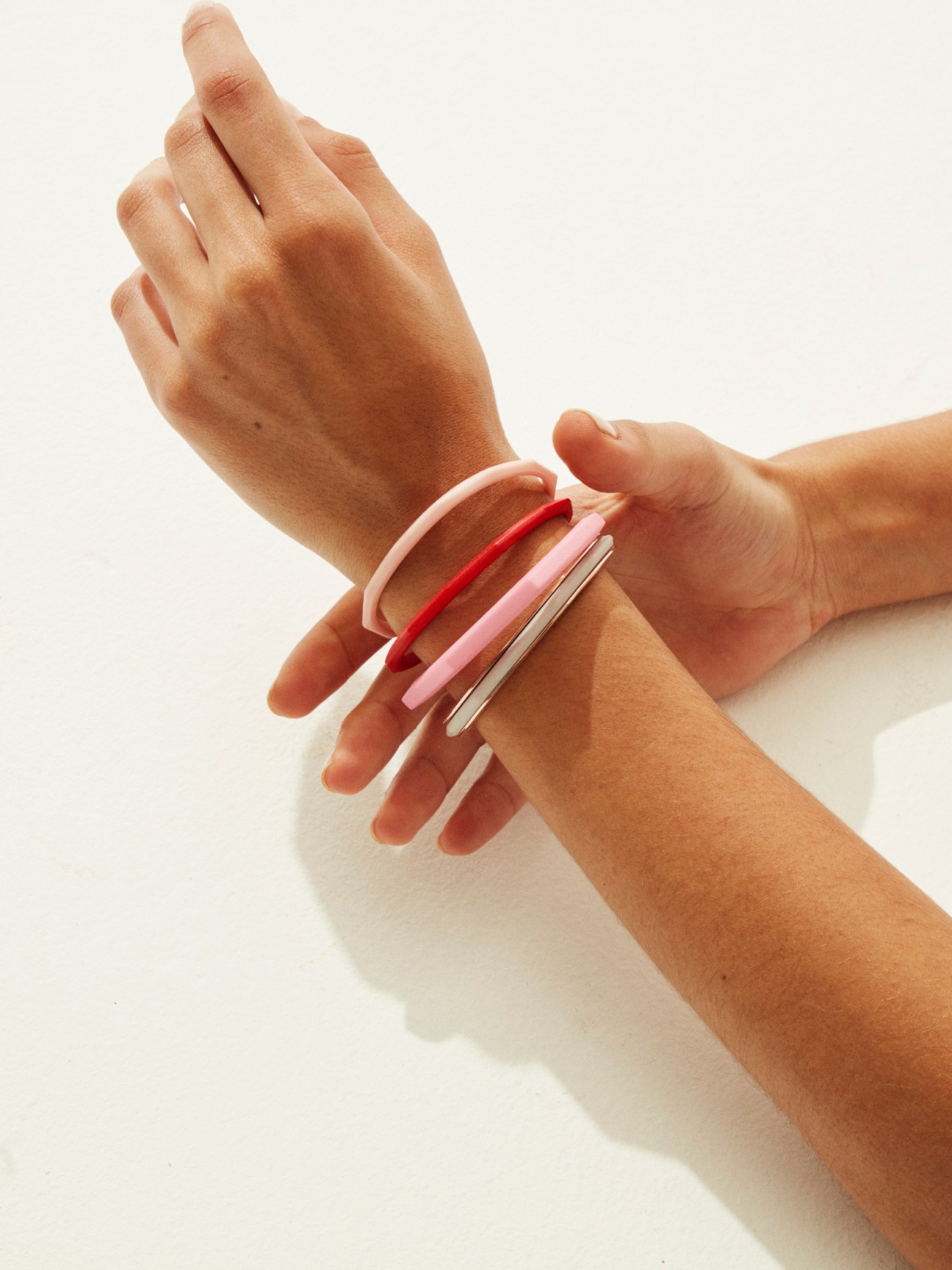 Model's wrist displaying four colorful bangles in pink, red, and metallic shades by Nyyukin.