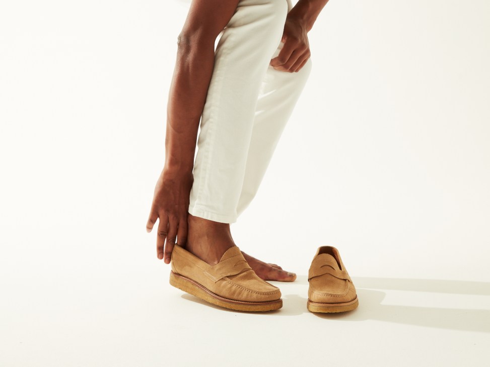Person wearing cream jeans and tan suede loafers against white background.